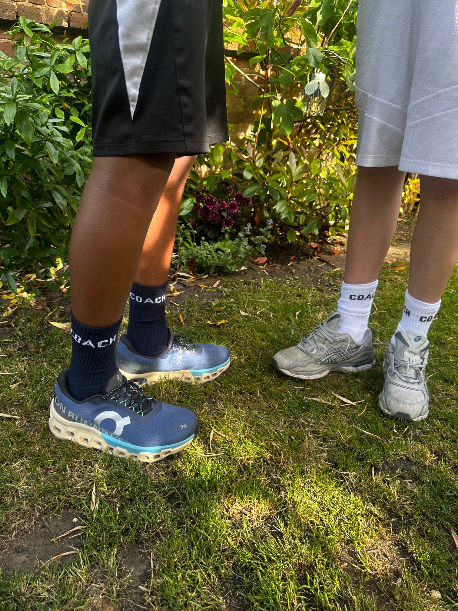 Two pairs of feet wearing Coach socks outdoors on grass